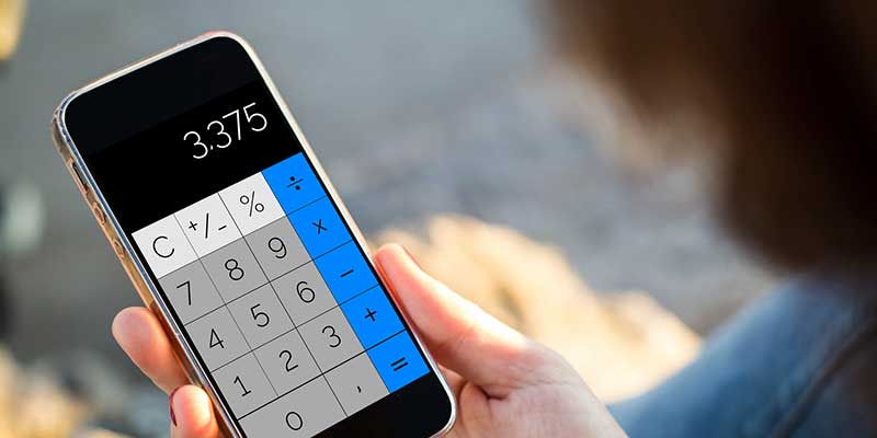 A hand holds a calculator with blue, white, and grey buttons on it. The display reads 3.375