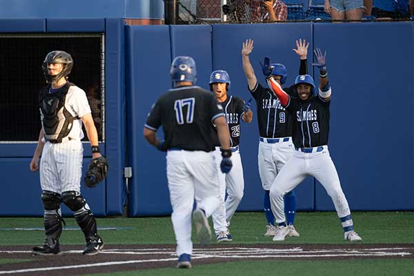 Baseball team members high five anther team member coming into home plate