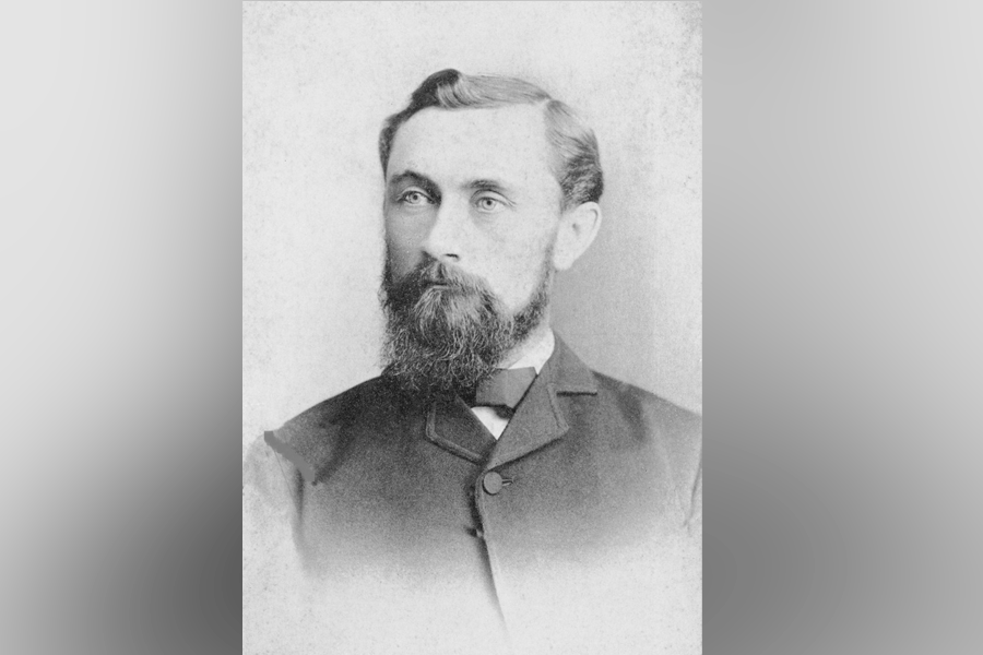 A black-and-white photograph of a man (President William Albert Jones) with short hair and a full beard and mustache. He looks ahead and to the left. He wears a button-up suit with a bowtie. A grey border is around the photograph.&nbsp;