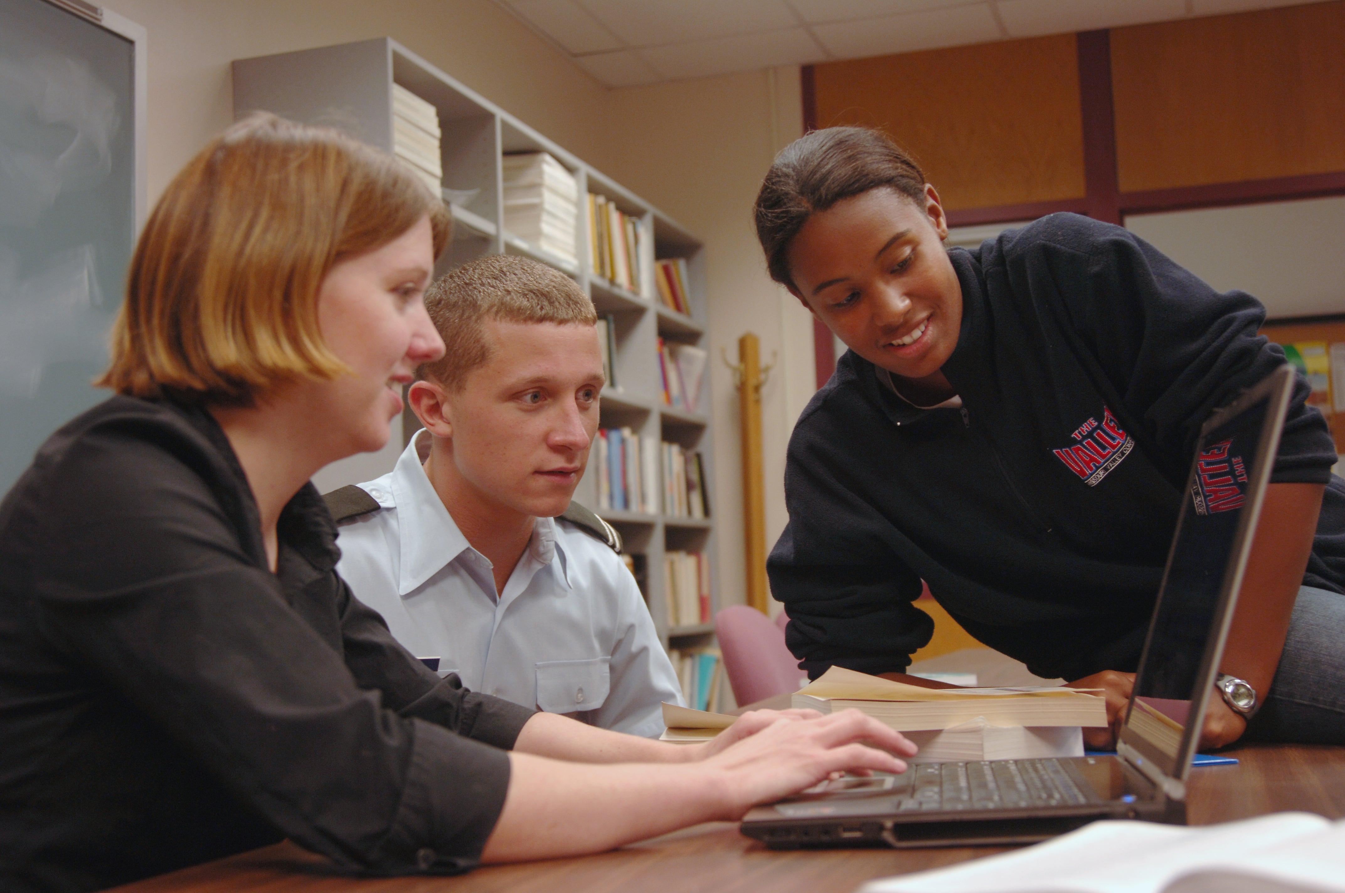 Three people collaborating on a laptop computer.