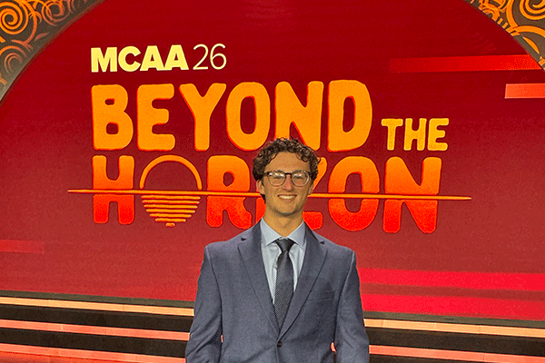 Male wearing a suit and glasses stands in front of a red display with the words “Beyond the Horizon” in large orange letters.
