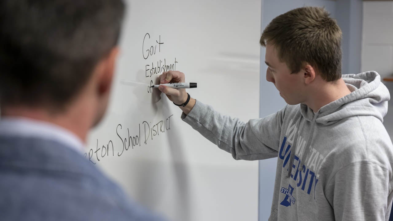 Student writes on a classroom whiteboard during a discussion.