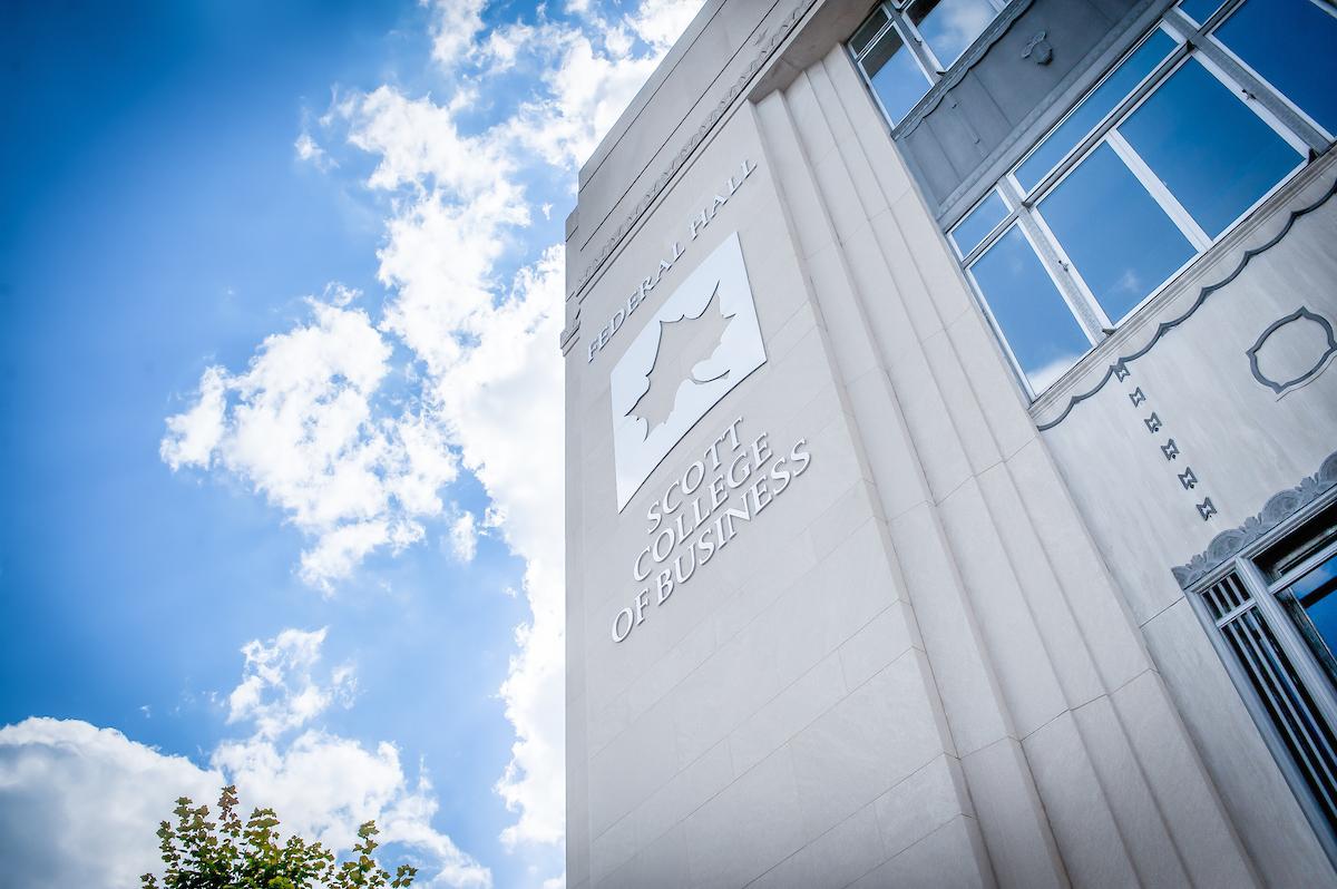 Exterior wall of Federal Hall at Scott College of Business with logo and windows under a partly cloudy blue sky.