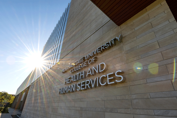 An exterior view of the College of Health and Human Services building, a brick building with glass windows on the left side of the building. “Indiana State University College of Health and Human Services” lettering is on the front side. Green trees are to the left of the building.