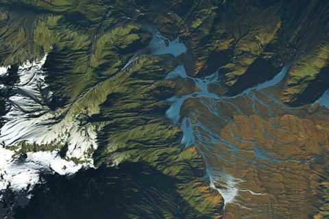 An aerial view of a map showing the landscape of a mountain region, with dark green and brown colors. White clouds are visible on the map, as well as blue water streams.  