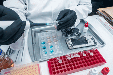 Detail photo a person working in a lab with a white lab coat and gloves working on a phone damaged by fire. 