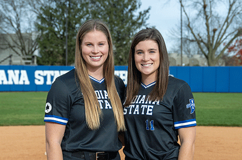 “Portrait of two women wearing matching black athletic jerseys, standing outdoors on a sports field.”