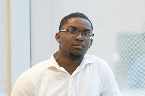 “Portrait of a man wearing glasses and a white shirt, seated indoors against a light background.”