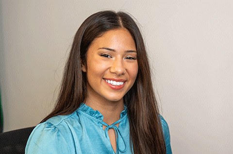 “Portrait of a woman wearing a blue blouse, smiling indoors against a light background.”