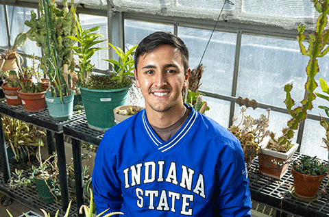 “Portrait of a man wearing a blue Indiana State sweatshirt, seated indoors with plants visible in the background.”