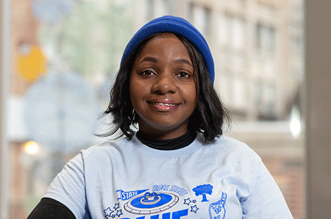 “Portrait of a woman wearing a blue hat and a light-colored T-shirt, smiling indoors with a softly blurred background.”