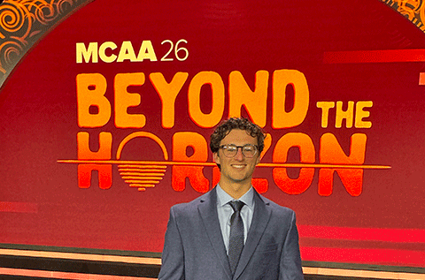 Male wearing a suit and glasses stands in front of a red display with the words “Beyond the Horizon” in large orange letters.