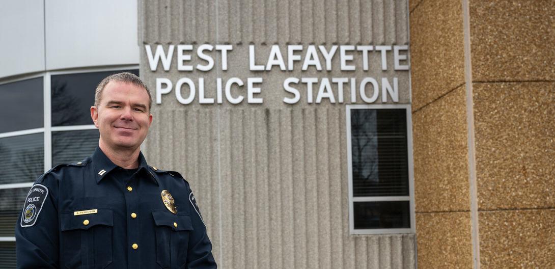 A white male in a police uniform stands in front of the West Lafayette Police Station building. The building’s name is prominently displayed in large letters.